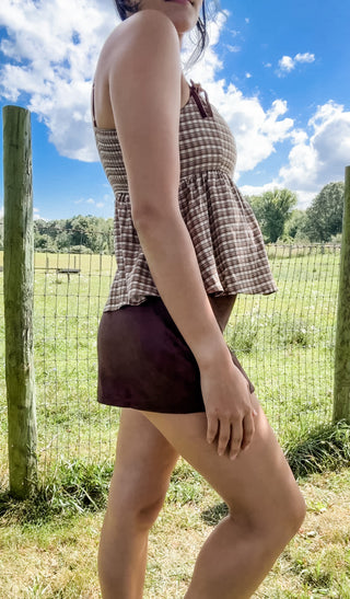 Brown gingham peplum tank with bow-tie straps paired with a chocolate brown mini skirt, side profile view.