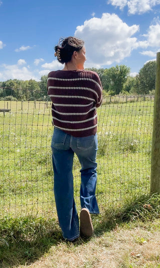 Brown ribbed sweater with white horizontal stripes paired with relaxed blue jeans, shown from the back outdoors.