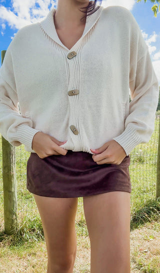 Woman wearing cream button-front cardigan with shawl collar and brown mini skirt, cozy chic boutique fall outfit